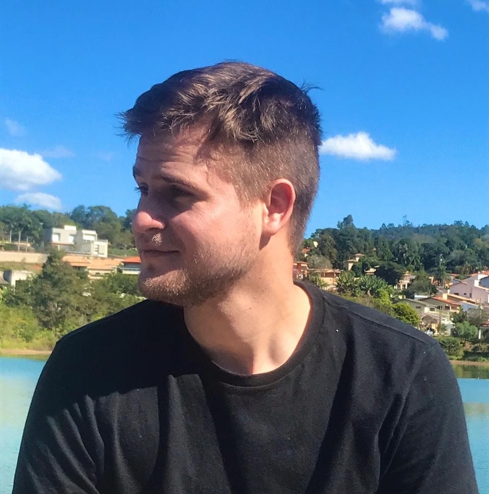 Autor sentado ao ar livre olhando para o horizonte, com uma expressão feliz em seus rosto